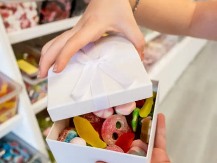 Hands opening a box filled with colorful gummy candies at a store.